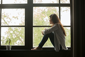 a woman sitting by herself looking out of a window who needs to contact addiction recovery help for her anxiety