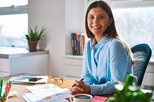 woman smiling at her desk with a blue shirt at her job
