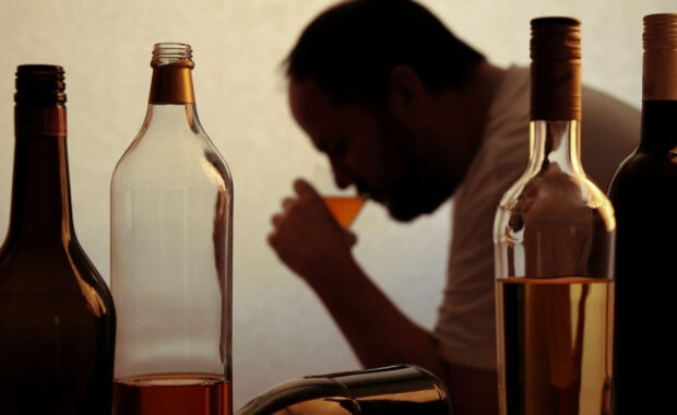 silhouette of anonymous alcoholic person drinking behind bottles of alcohol