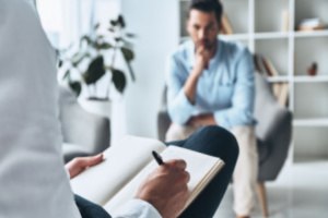 A therapist is writing instructions for the patient sitting in front of him in the afterlife of an intensive outpatient program