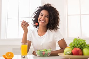 A black woman having a healthy breakfast which includes fruits, juice, and salad