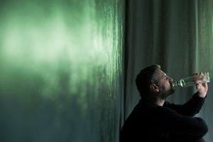 An man drinking sitting next to wall