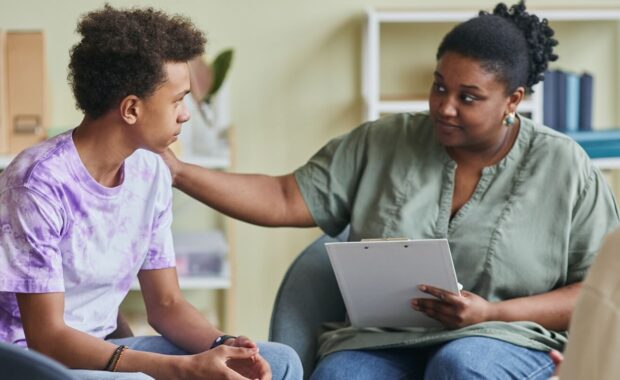 african young psychologist talking to teenage boy during CBT therapy session at classroom in DC