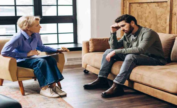 Young Man Sitting on A Couch Talking to Female Therapist about His Childhood Trauma